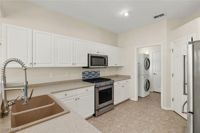 kitchen featuring stainless steel appliances, stacked washer and clothes dryer, white cabinets, and sink