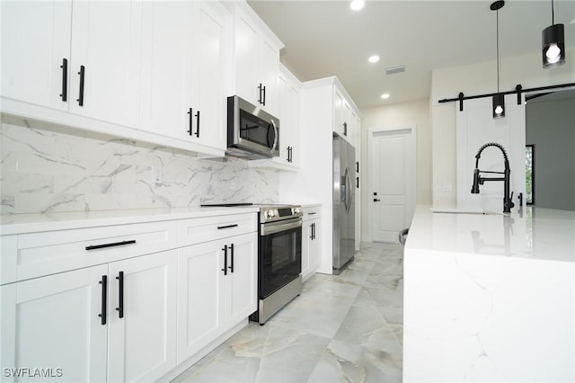 kitchen with light stone counters, pendant lighting, stainless steel appliances, a barn door, and white cabinets