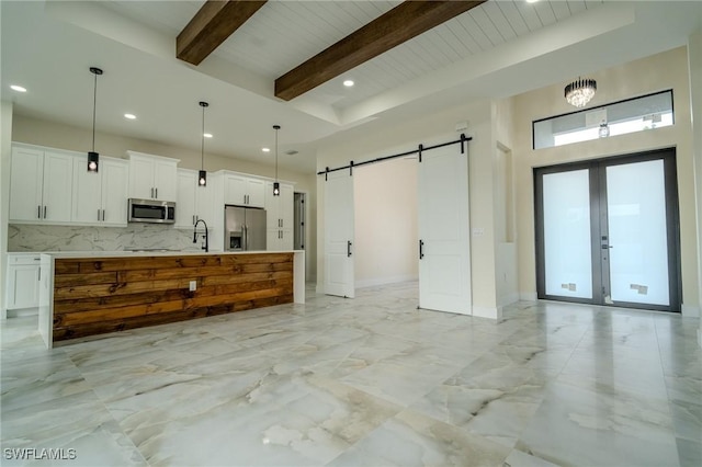 kitchen featuring appliances with stainless steel finishes, pendant lighting, a barn door, a kitchen island with sink, and white cabinets