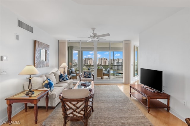 living room with ceiling fan, wood finished floors, visible vents, baseboards, and expansive windows