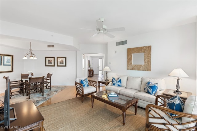 living room featuring ceiling fan with notable chandelier, visible vents, baseboards, and wood finished floors