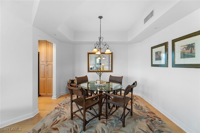 dining space with light wood-style flooring, a raised ceiling, visible vents, and baseboards