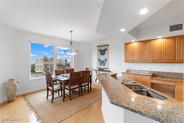 kitchen with a view of city, pendant lighting, visible vents, light wood-style flooring, and a sink