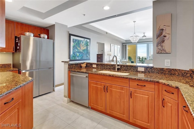 kitchen featuring sink, appliances with stainless steel finishes, a tray ceiling, decorative light fixtures, and dark stone counters