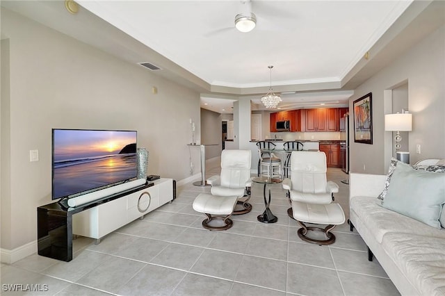 living room with crown molding, a notable chandelier, a tray ceiling, and light tile patterned floors