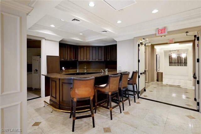 kitchen with a kitchen bar, dark brown cabinets, ornamental molding, kitchen peninsula, and white fridge with ice dispenser