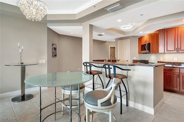 kitchen featuring light tile patterned flooring, dark stone countertops, crown molding, and a breakfast bar area