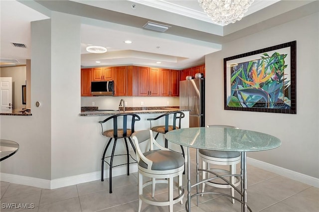 dining area with a kitchen breakfast bar, light tile patterned floors, a raised ceiling, and kitchen peninsula
