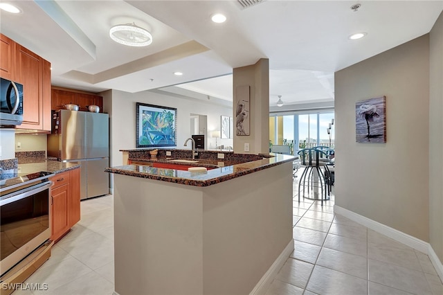 kitchen with light tile patterned floors, stainless steel appliances, dark stone counters, and sink