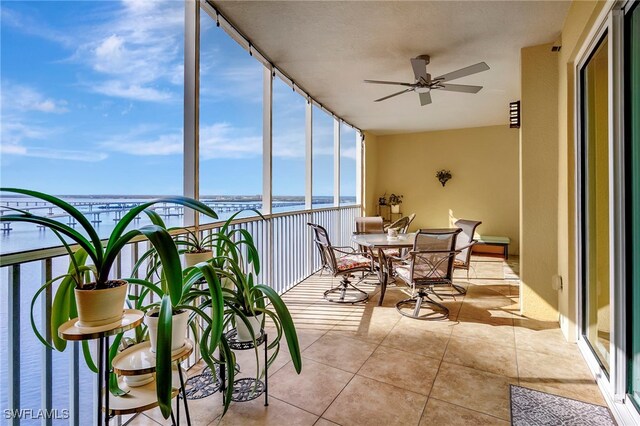 sunroom with ceiling fan and a water view