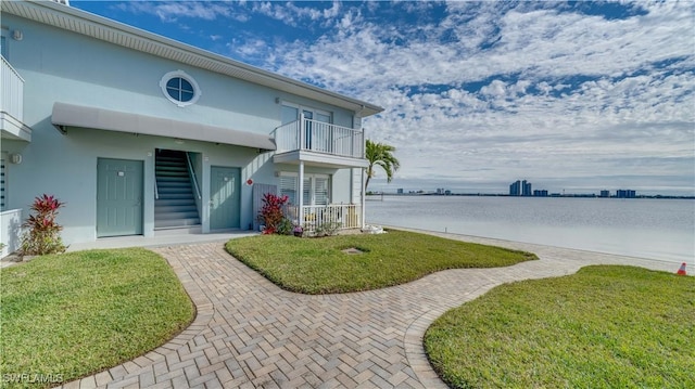 view of front facade featuring a front yard, a balcony, and a water view