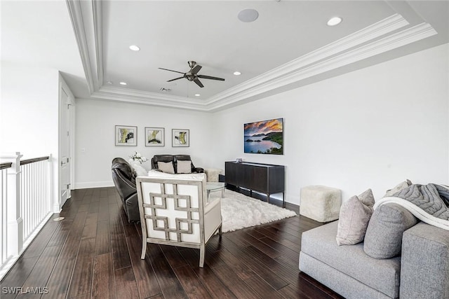 living room featuring ceiling fan, a tray ceiling, dark hardwood / wood-style flooring, and crown molding