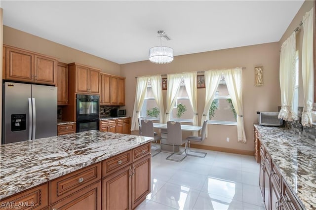 kitchen with black double oven, light stone countertops, hanging light fixtures, plenty of natural light, and stainless steel fridge