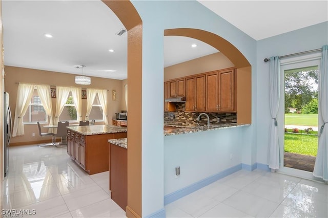 kitchen with kitchen peninsula, decorative light fixtures, a wealth of natural light, light stone counters, and decorative backsplash