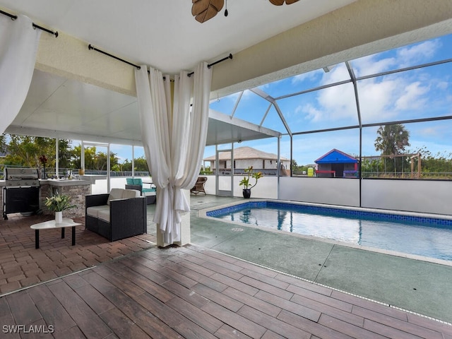 view of swimming pool with an outdoor kitchen, a patio area, grilling area, glass enclosure, and ceiling fan