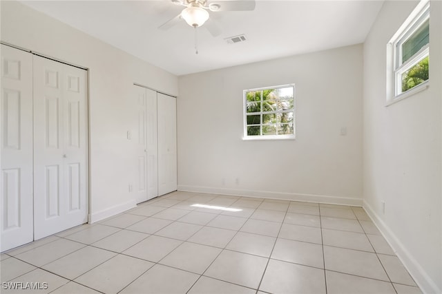 unfurnished bedroom featuring light tile patterned floors, multiple closets, and ceiling fan