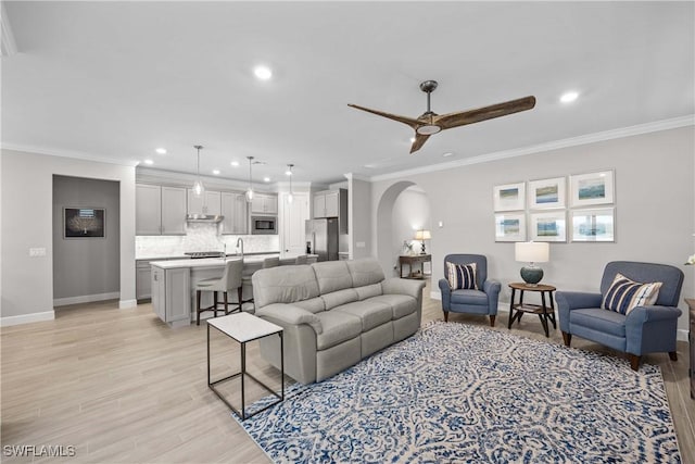 living room with ornamental molding, ceiling fan, and light wood-type flooring