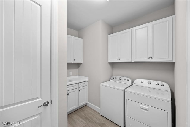 washroom with separate washer and dryer, light hardwood / wood-style floors, and cabinets