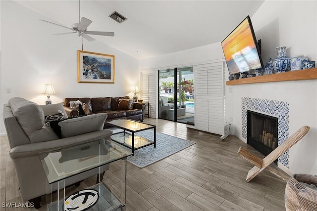 living room featuring a tiled fireplace, vaulted ceiling, and ceiling fan