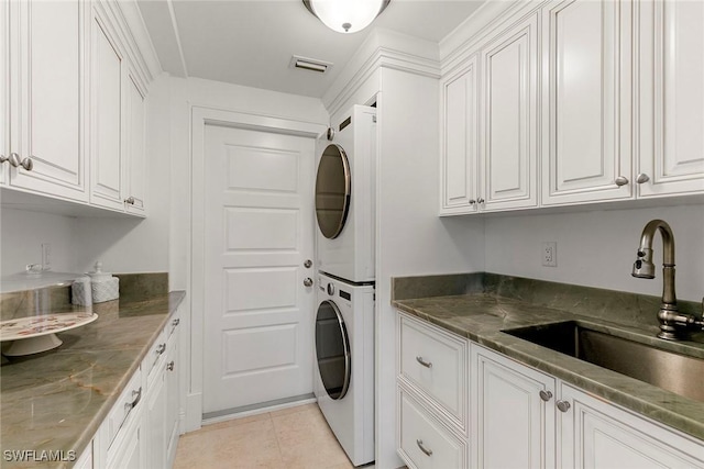 laundry area featuring sink, light tile patterned floors, cabinets, and stacked washing maching and dryer