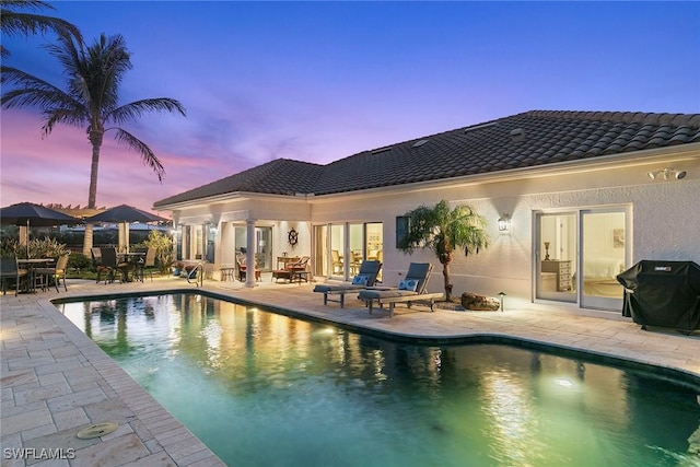 pool at dusk with area for grilling and a patio area