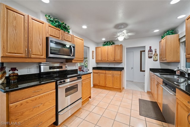 kitchen with sink, light tile patterned floors, ceiling fan, appliances with stainless steel finishes, and dark stone counters