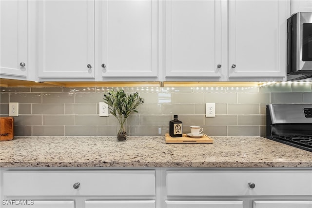 kitchen featuring gas stove, decorative backsplash, light stone countertops, and white cabinetry