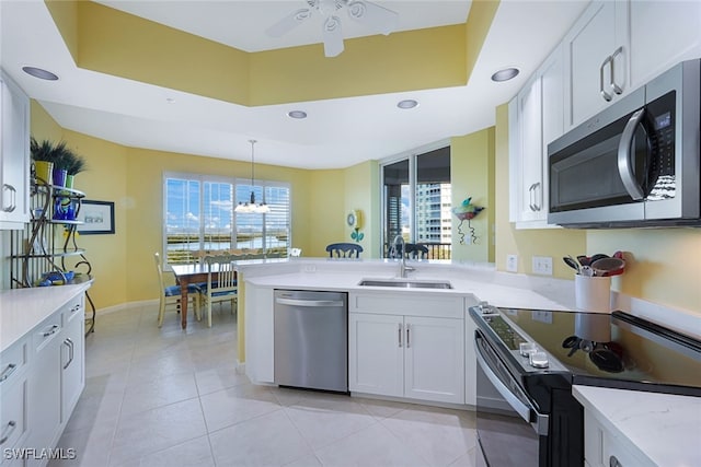 kitchen featuring white cabinetry, stainless steel appliances, a tray ceiling, and hanging light fixtures