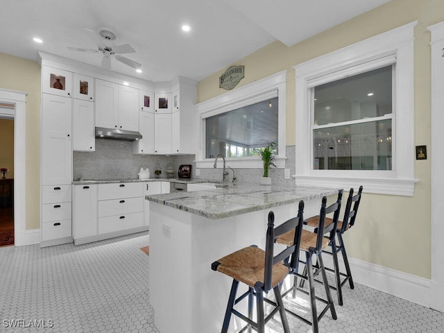 kitchen featuring sink, white cabinets, a kitchen breakfast bar, light stone counters, and kitchen peninsula