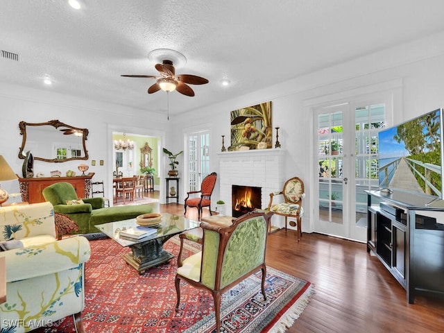 living room with dark hardwood / wood-style floors, ceiling fan with notable chandelier, a fireplace, a textured ceiling, and french doors