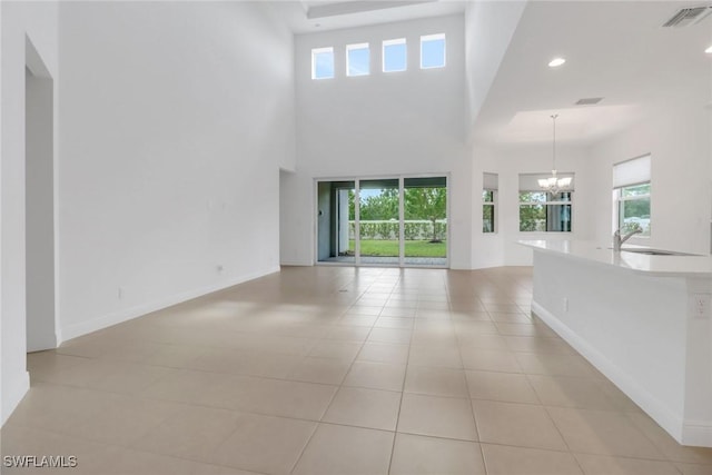 unfurnished living room featuring a healthy amount of sunlight, sink, light tile patterned floors, and a chandelier