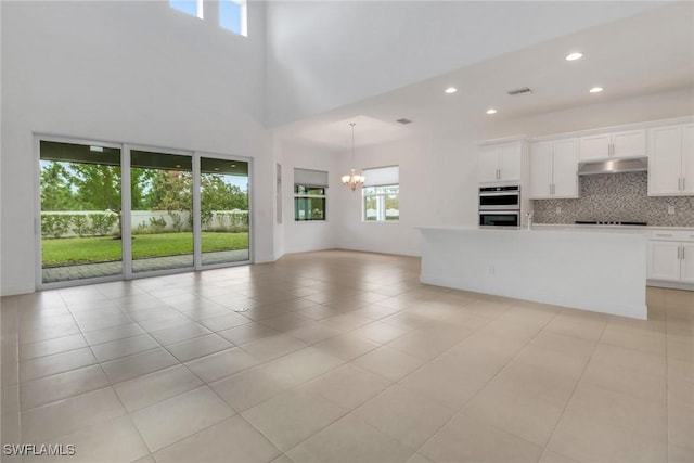 kitchen with an inviting chandelier, double oven, white cabinets, light tile patterned flooring, and decorative backsplash