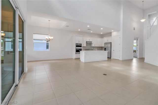 unfurnished living room with light tile patterned flooring, a towering ceiling, and a chandelier