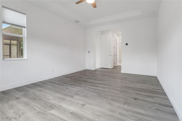 empty room with a tray ceiling, ornamental molding, light hardwood / wood-style floors, and ceiling fan
