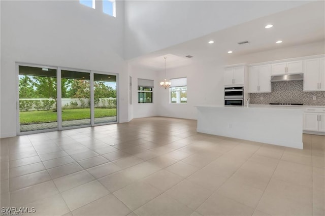 kitchen featuring white cabinetry, an inviting chandelier, tasteful backsplash, double oven, and a kitchen island