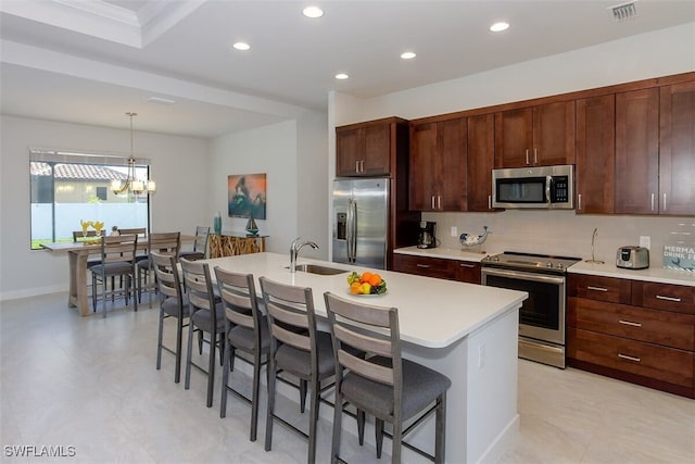 kitchen with decorative light fixtures, stainless steel appliances, an island with sink, sink, and a kitchen breakfast bar