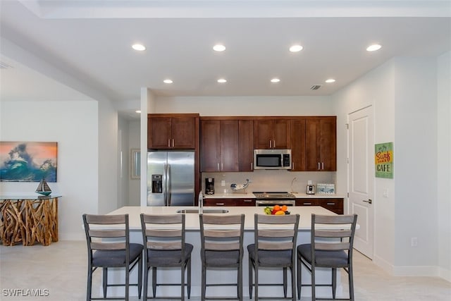 kitchen with a kitchen bar, appliances with stainless steel finishes, a kitchen island with sink, dark brown cabinetry, and sink