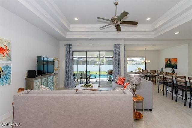 living room featuring crown molding, ceiling fan with notable chandelier, and a tray ceiling