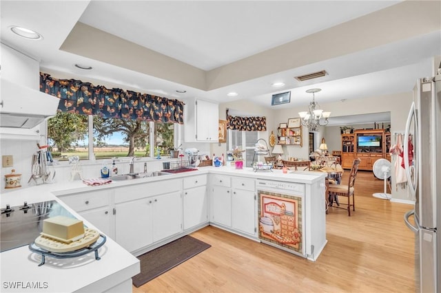 kitchen featuring white cabinets, hanging light fixtures, stainless steel fridge, kitchen peninsula, and light wood-type flooring