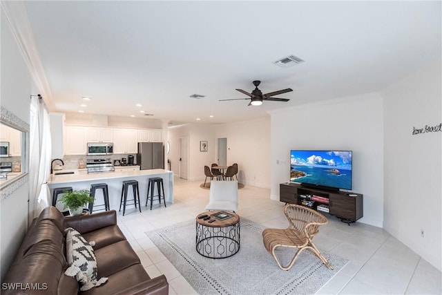 living room with ceiling fan, sink, light tile patterned floors, and ornamental molding