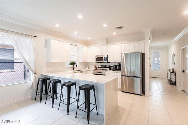 kitchen featuring kitchen peninsula, a kitchen bar, sink, appliances with stainless steel finishes, and white cabinets