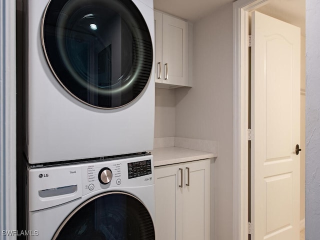 clothes washing area with cabinets and stacked washer / dryer