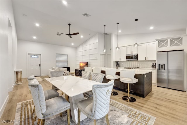 dining space featuring ceiling fan, high vaulted ceiling, and light wood-type flooring