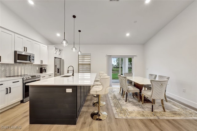 kitchen with pendant lighting, tasteful backsplash, stainless steel appliances, and a center island with sink