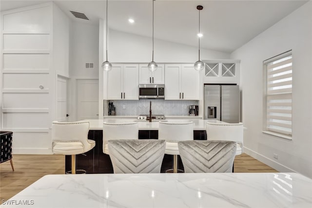 kitchen with white cabinetry, light stone counters, appliances with stainless steel finishes, pendant lighting, and decorative backsplash