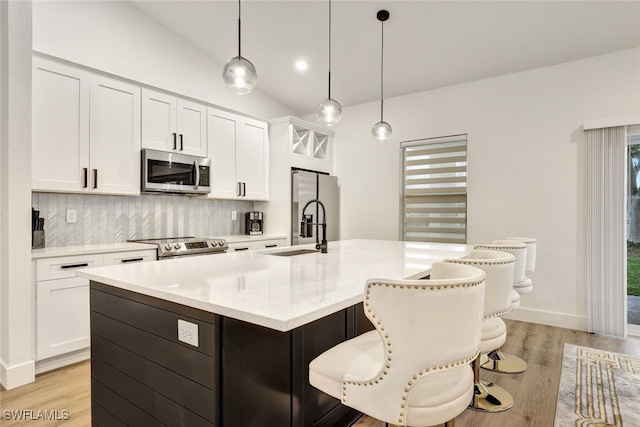 kitchen with pendant lighting, an island with sink, white cabinets, and appliances with stainless steel finishes