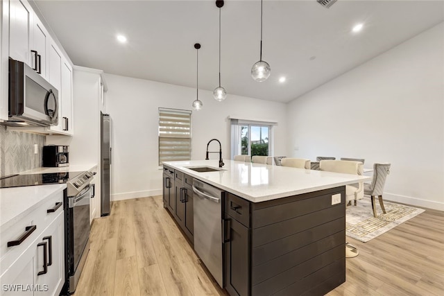 kitchen with sink, white cabinetry, decorative light fixtures, light wood-type flooring, and stainless steel appliances