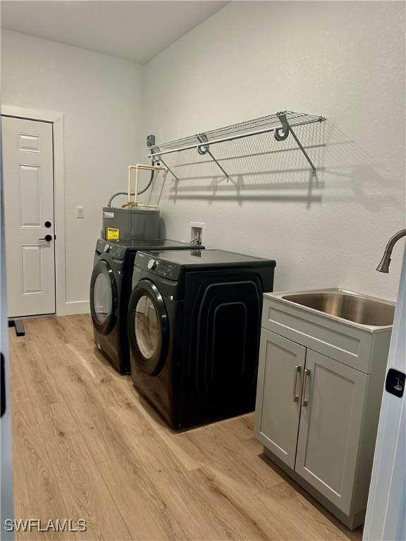 clothes washing area with water heater, sink, cabinets, washing machine and dryer, and light wood-type flooring