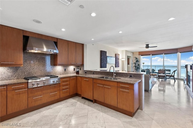 kitchen featuring sink, a water view, stainless steel gas cooktop, kitchen peninsula, and wall chimney exhaust hood