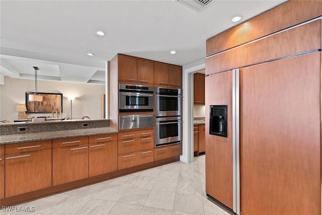 kitchen featuring double oven, paneled refrigerator, pendant lighting, and dark stone counters